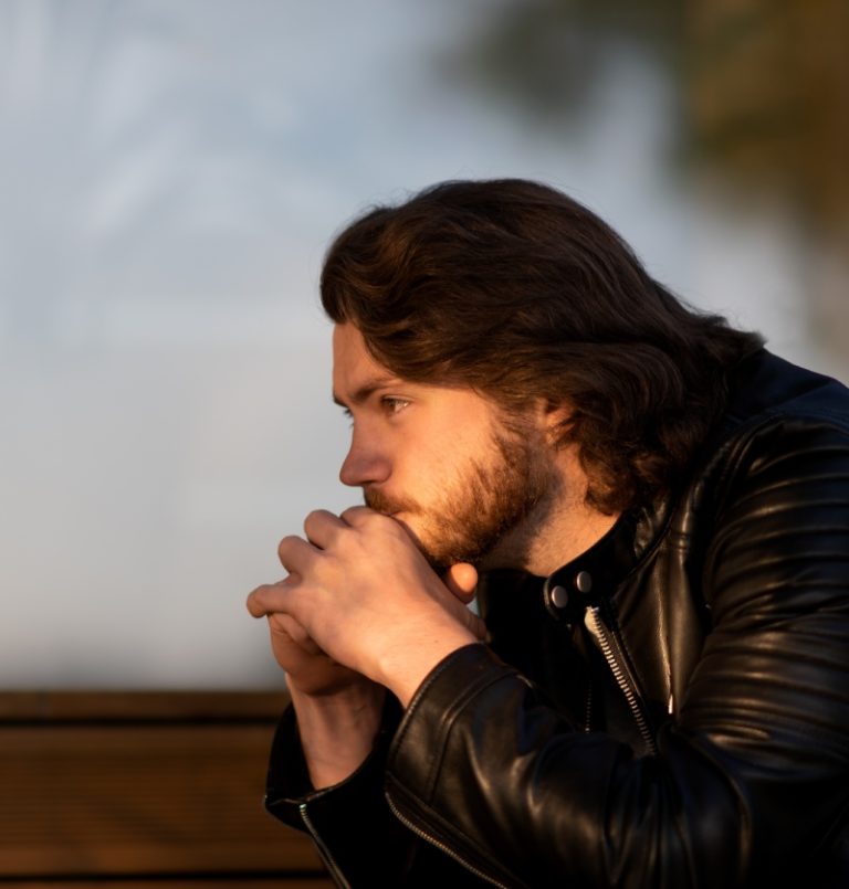 A contemplative man in civilian clothes reflecting outdoors, representing trauma and PTSD support for veterans and first responders in New Jersey