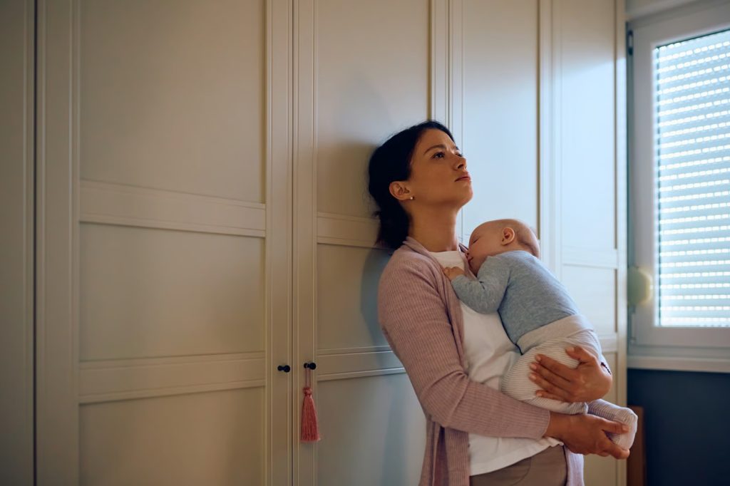 A mother holding her baby closely while looking pensive, illustrating the difference between new mom stress and postpartum anxiety in Voorhees, NJ.